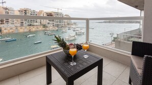 A balcony with a wicker table, two glasses of orange juice, and a bowl of fruit.