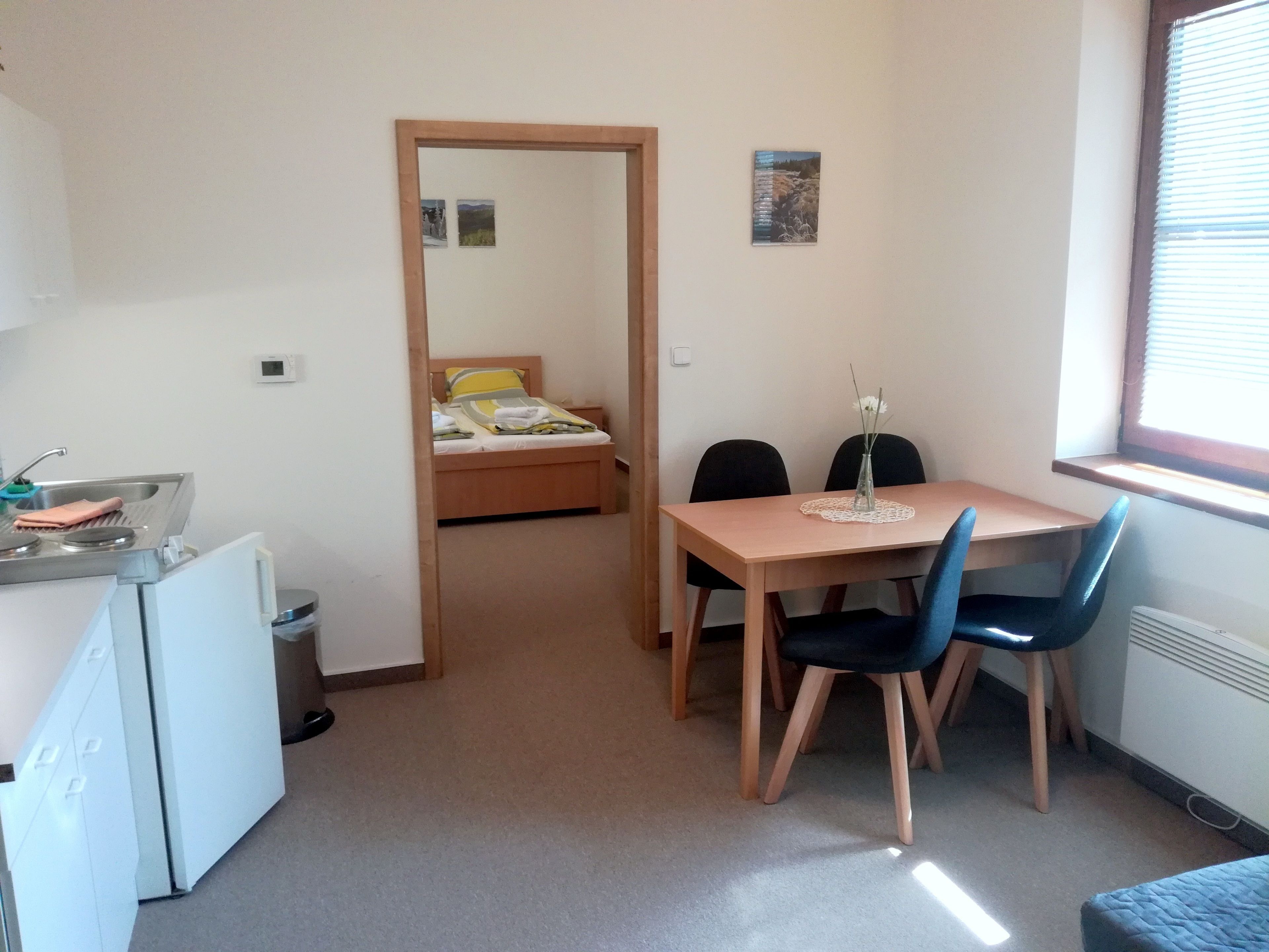 Una habitación compacta con cama, una pequeña kitchenette, una mesa de comedor con sillas y una ventana.