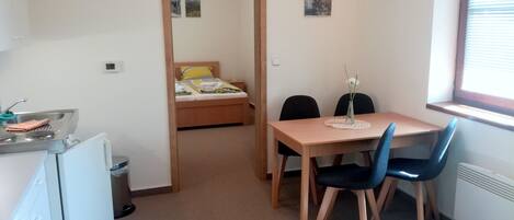Una habitación compacta con cama, una pequeña kitchenette, una mesa de comedor con sillas y una ventana.