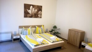 A bedroom with a bed, bedside tables, a nightstand, a potted plant, and a wooden cabinet.