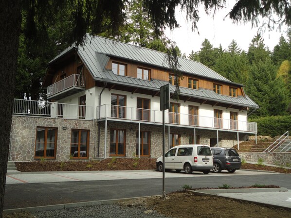 A two-story building with a stone facade, wooden balconies, and a car parked in front.
