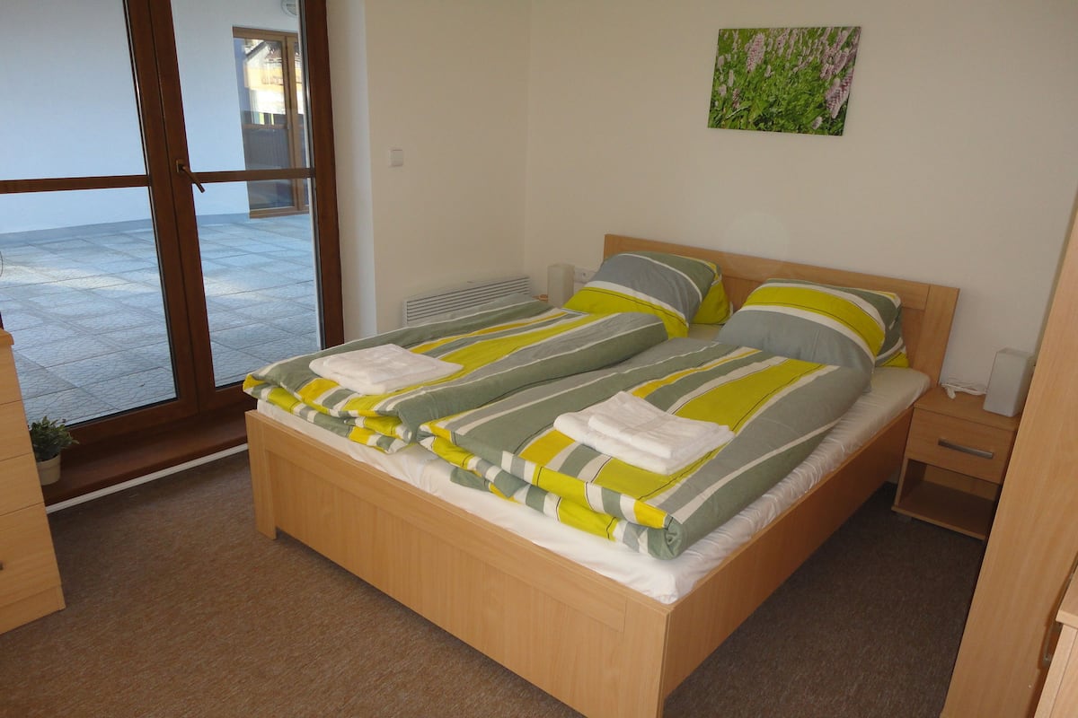 A bedroom with a wooden bed, a bedside table, and a window with a view of the outside.