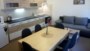 A compact kitchen with a dining area, a grey sofa, and a small table with chairs.