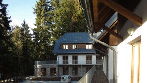 A wooden deck with a railing, a building with a stone facade, and a vehicle parked in the background.