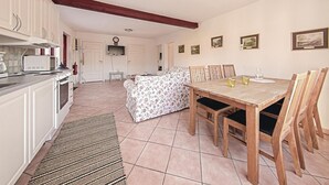 A spacious kitchen with white cabinets, a microwave, and a stove. There is a dining area with a wooden table and chairs, and a sofa in the background. - 3 bedroom cozy home in Tomelilla (Tomelilla)