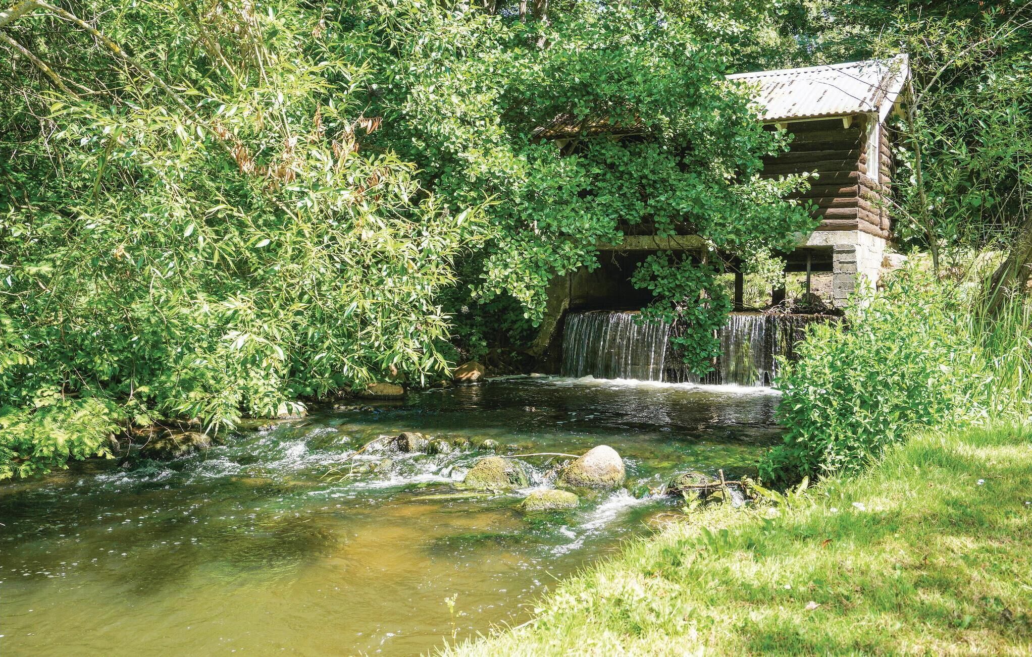A rustic stone building with a small waterfall, surrounded by lush greenery.