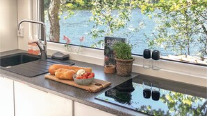 Cuina amb vista a un llac, una taula de tall amb pa i tomàquets, i una planta en test.