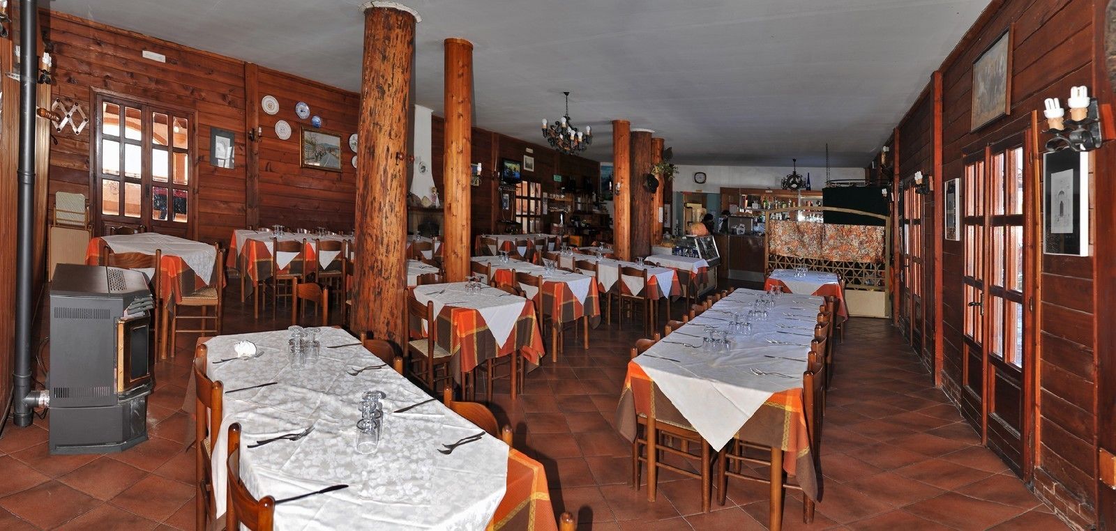 Un interior rústico de madera con varias mesas preparadas para comer, grandes pilares de madera y un horno de leña tradicional.