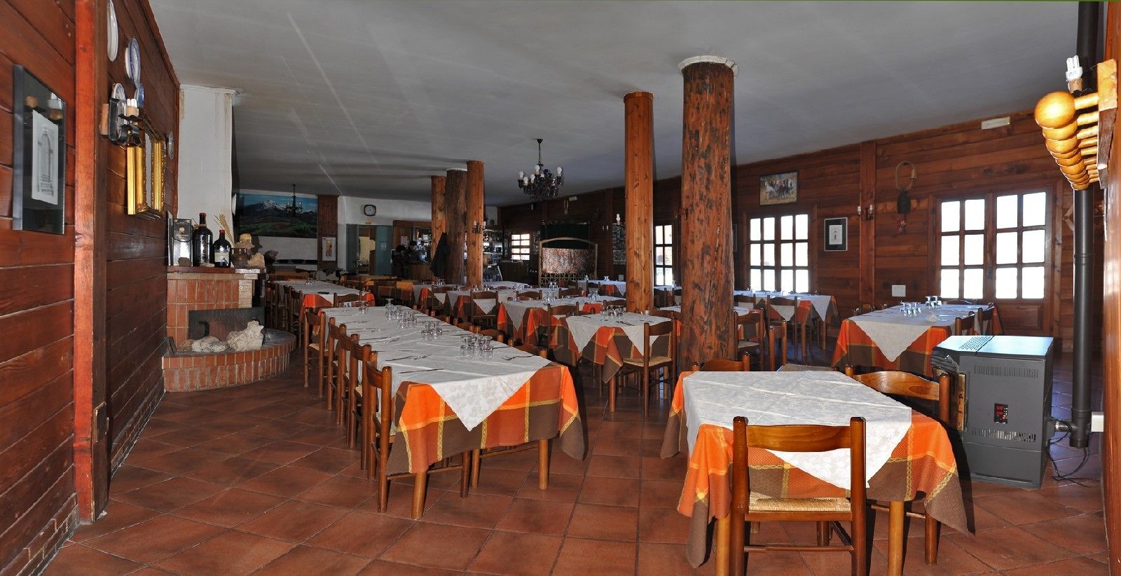 A restaurant with long tables, wooden pillars, and a tiled floor.