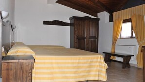 A bedroom with a wooden ceiling, a bed with a striped bedspread, a bedside table, a wardrobe, and a window with curtains. - Hotel Pietrapanna (Calvello)