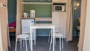 Una kitchenette compacta equipada con microondas, cafetera y refrigerador pequeño. Hay una mesa blanca con cuatro taburetes y una lámpara en la pared.