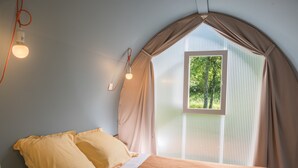 Un dormitorio con cama, ventana con cortinas y lámpara de pared.