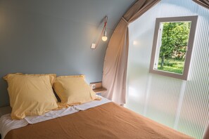 Ein Schlafzimmer mit einem Bett, zwei Kissen, einem Nachttisch, einer Lampe und einem Fenster mit Vorhängen.