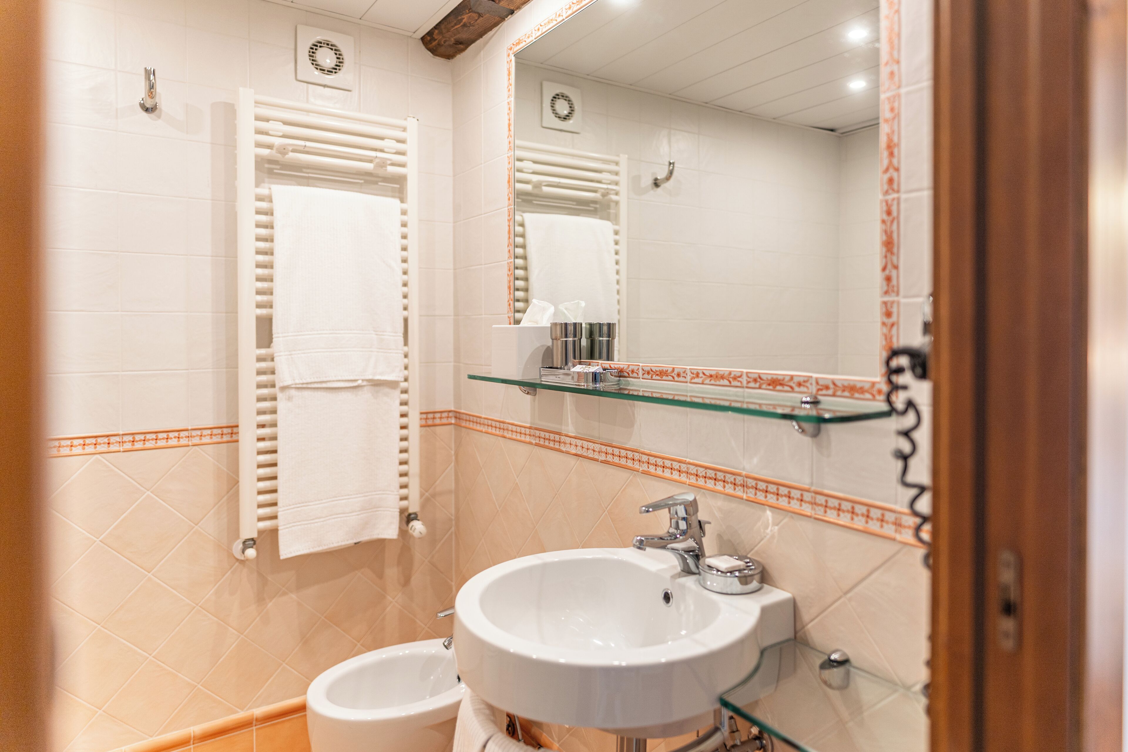 A bathroom with a white sink, a glass shelf above it, and a towel rack with towels.