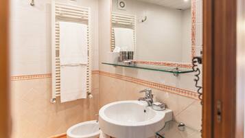 A bathroom with a white sink, a glass shelf above it, and a towel rack with towels.