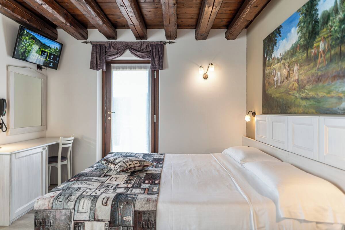 A bedroom with a bed, a desk, a chair, a television, and a painting on the wall.