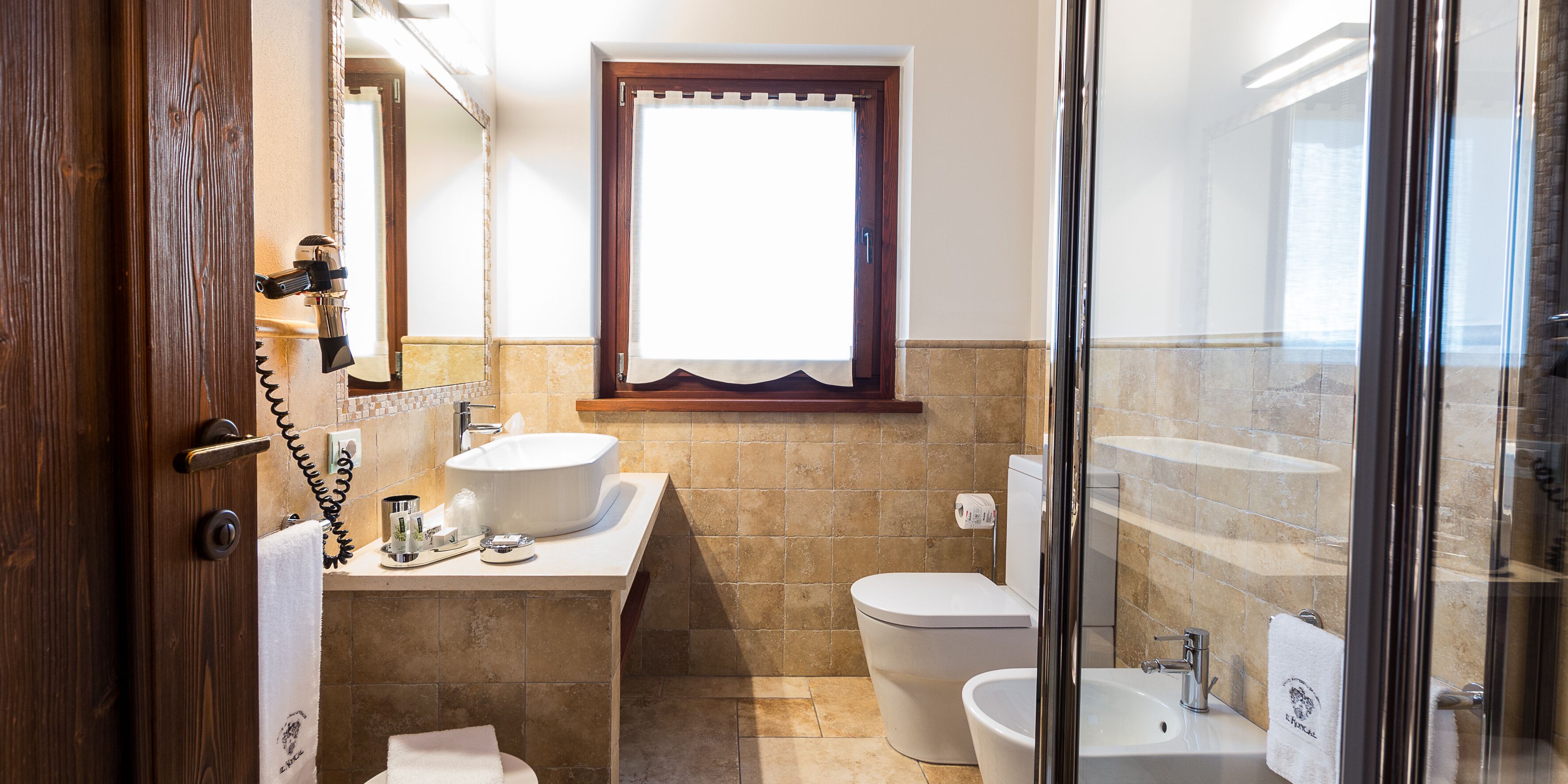 A bathroom with a sink, toilet, and bidet, a window, and a shower area.