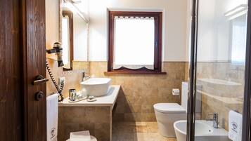 A bathroom with a sink, toilet, and bidet, a window, and a shower area.