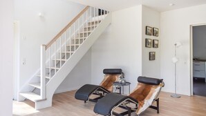 Een moderne woonkamer met een witte trap, twee relaxfauteuils, een klein tafeltje en ingelijste foto's aan de muur.