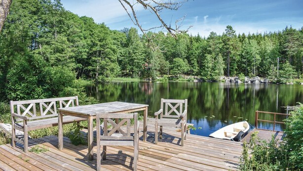 Een houten terras met een tafel en twee stoelen met uitzicht op een rustig meer, omgeven door dicht bos.