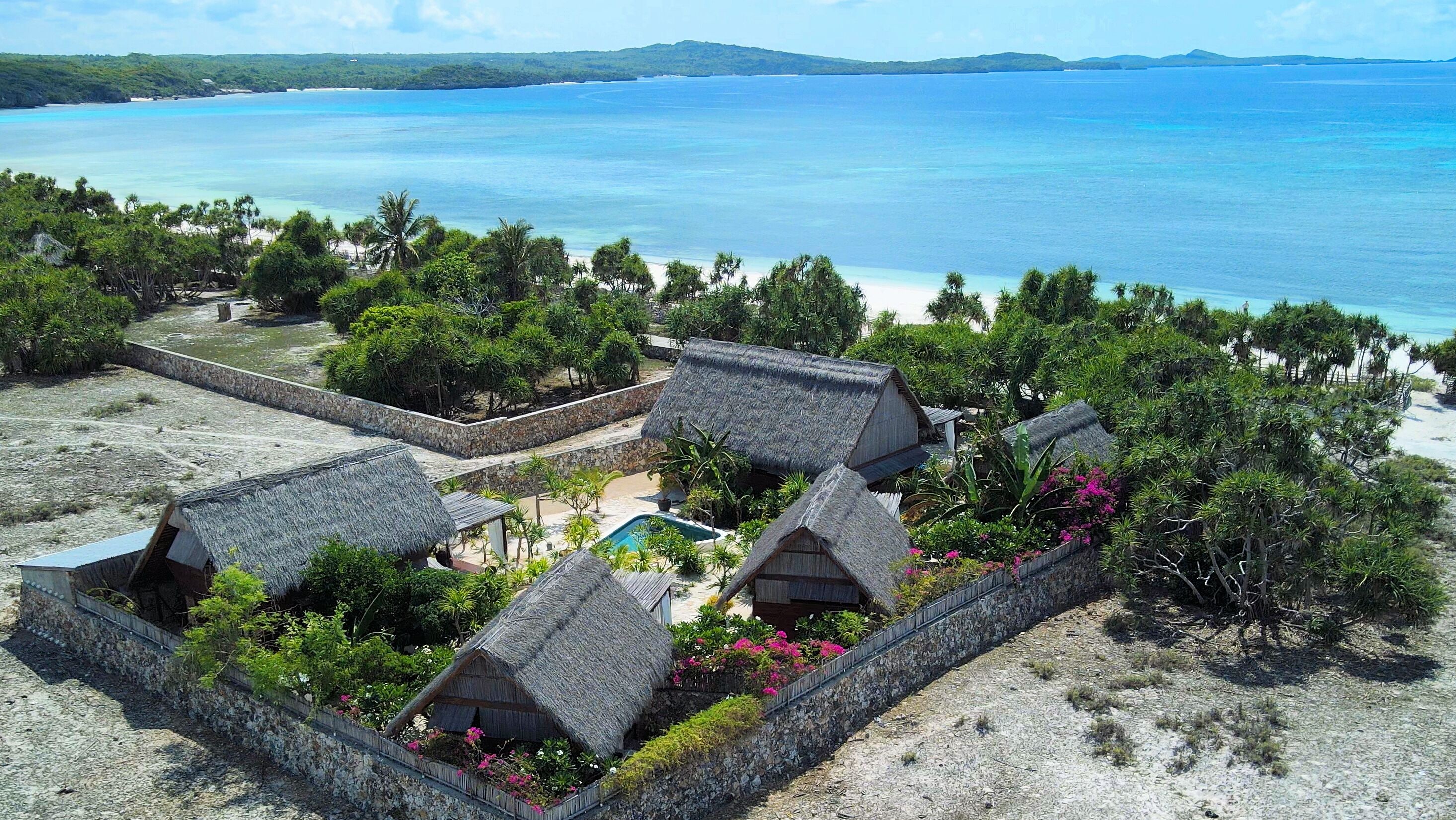 A resort with thatched-roof huts, a swimming pool, and a beach view.