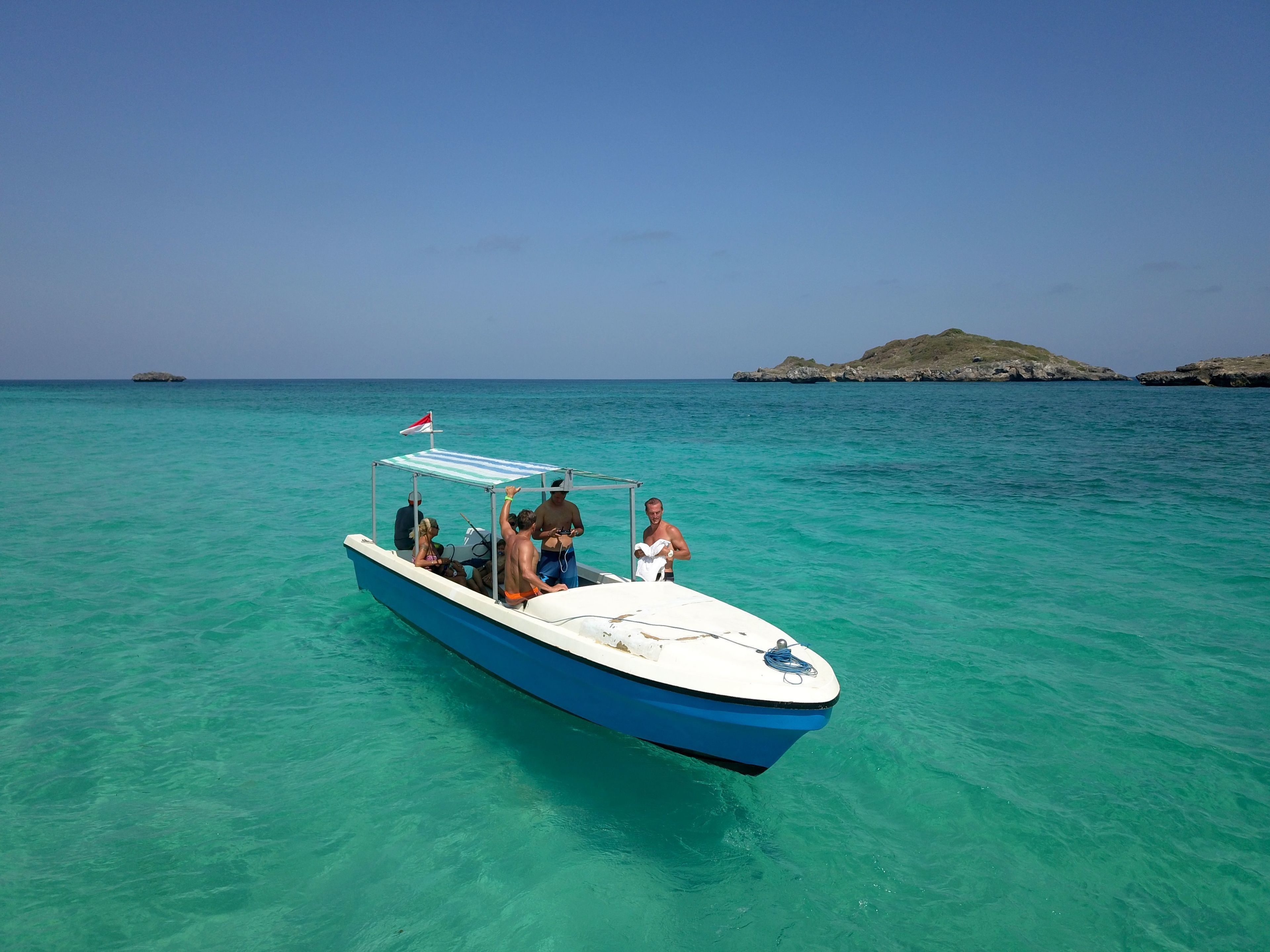 Um barco com passageiros, águas turquesa cristalinas e uma ilha rochosa ao fundo.