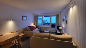 Habitación de hotel compacta con sofá, mesa de comedor y televisor.