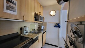 Cocina compacta con armarios de madera, microondas, cafetera y un lavabo.