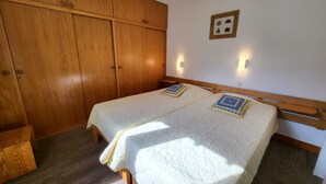 Un dormitorio con dos camas, armario de madera e iluminación en la pared.
