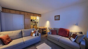 Un espacio habitable compacto con dos sofás, una mesita y una kitchenette al fondo.
