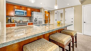 Una cocina con armarios de madera, electrodomésticos de acero inoxidable, encimera de granito y taburetes de bar.