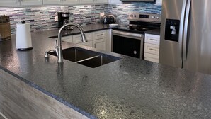 Eine moderne Küche mit weißen Schränken, einem Edelstahl-Kühlschrank, einer Mikrowelle und einer Arbeitsplatte aus Granit.