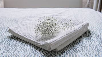 A neatly folded white towel on a bed with a blue and white patterned bedspread.