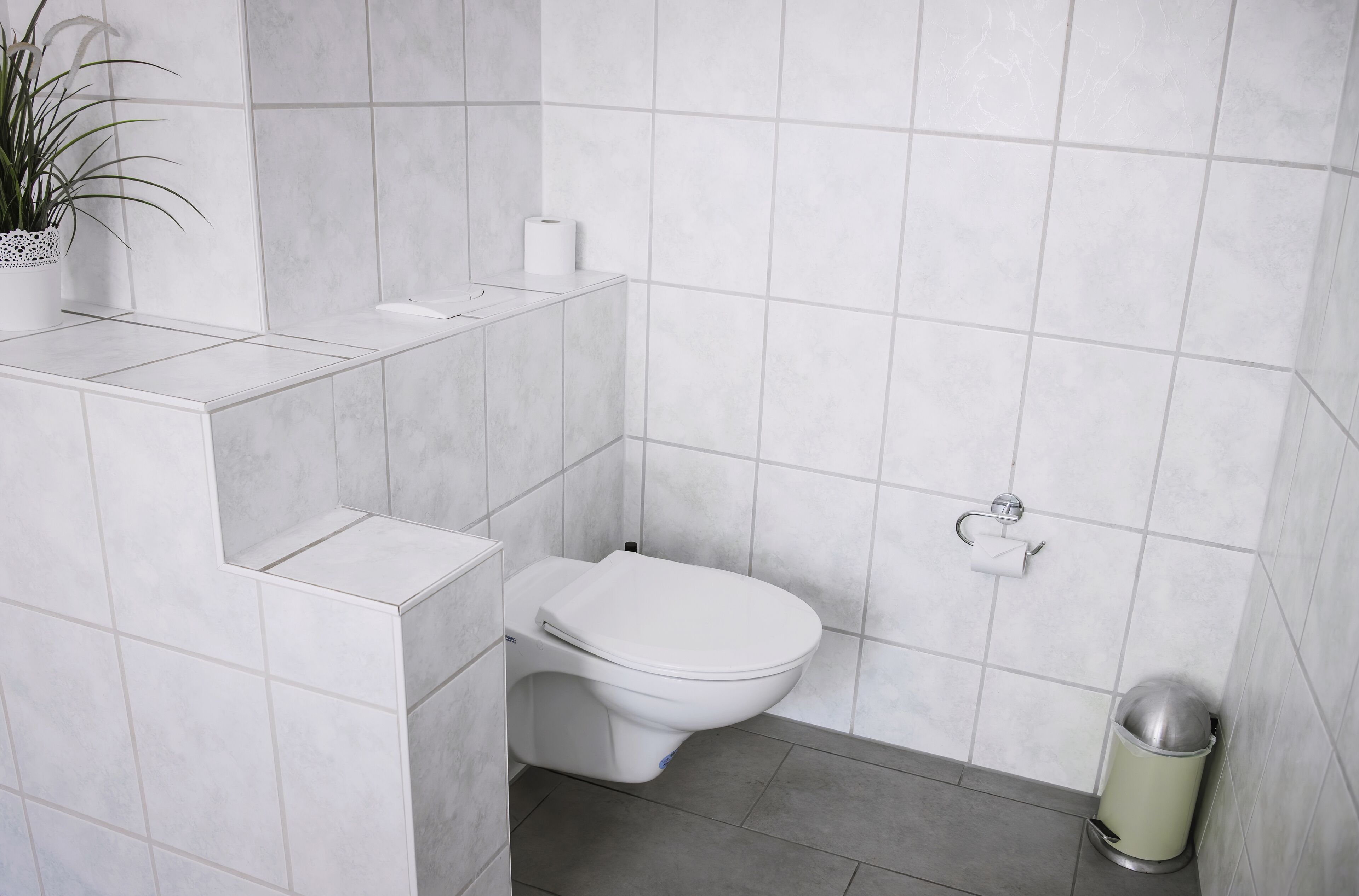 A bathroom with a toilet, a trash can, and a toilet paper holder on the wall.