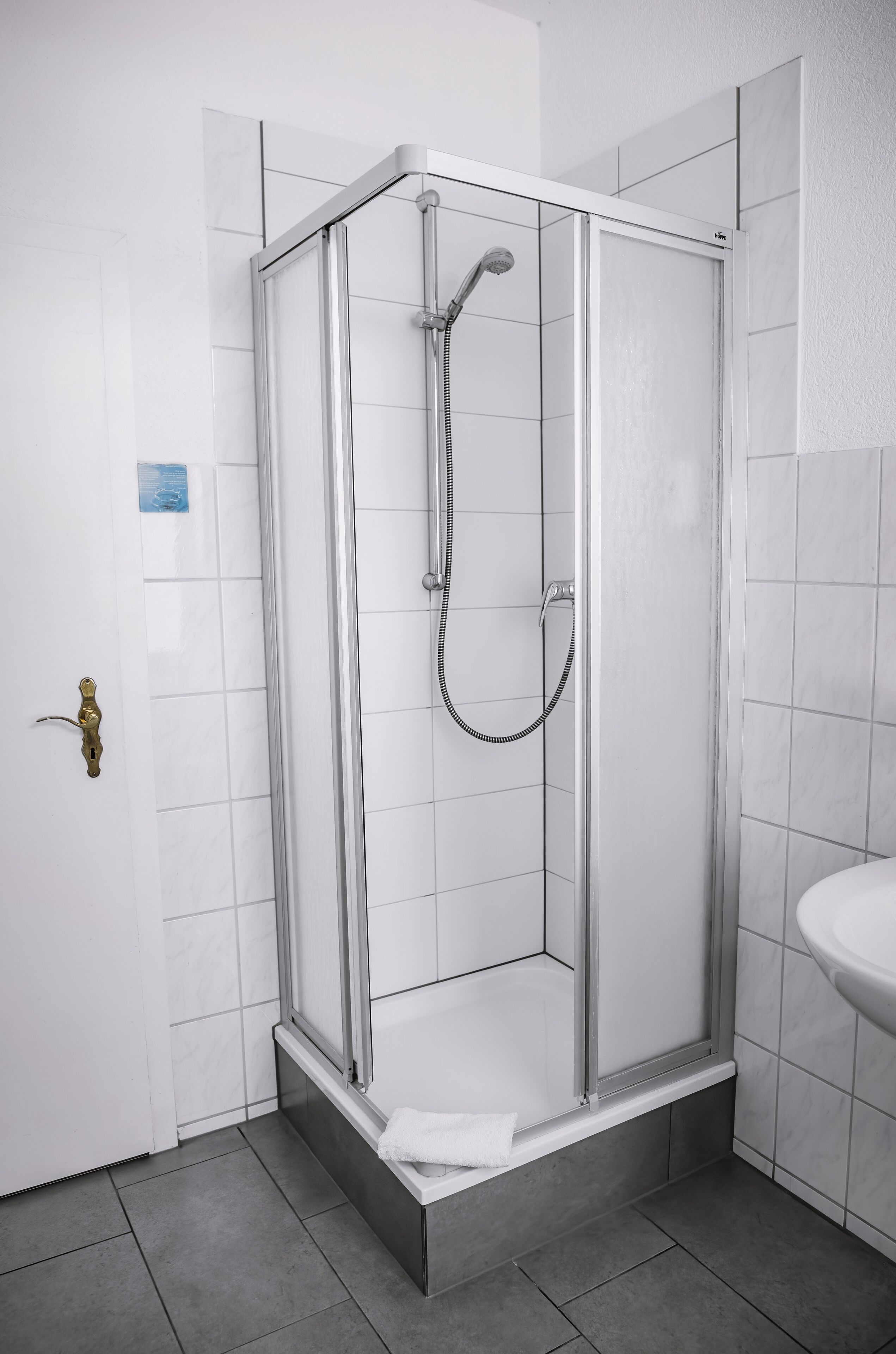 A modern bathroom with a glass-enclosed shower, a white sink, and a tiled floor.