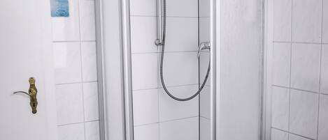 A modern bathroom with a glass-enclosed shower, a white sink, and a tiled floor.