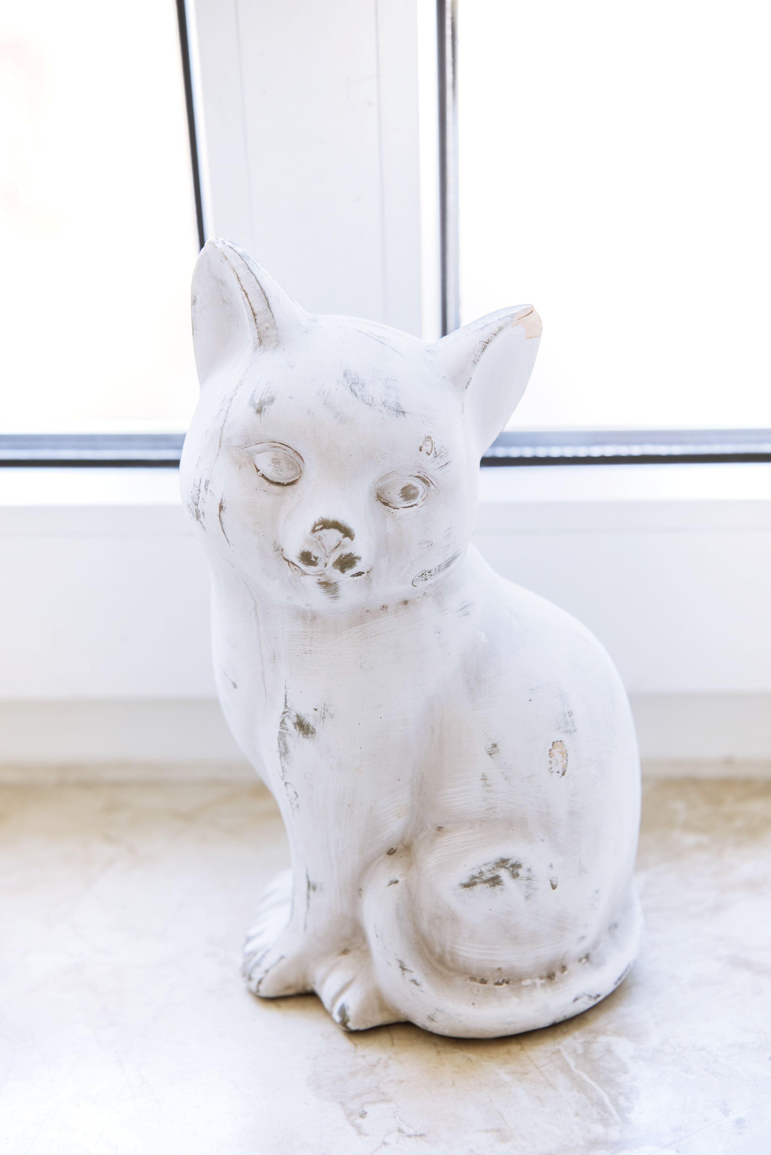A white ceramic cat sculpture on a marble floor near a window.