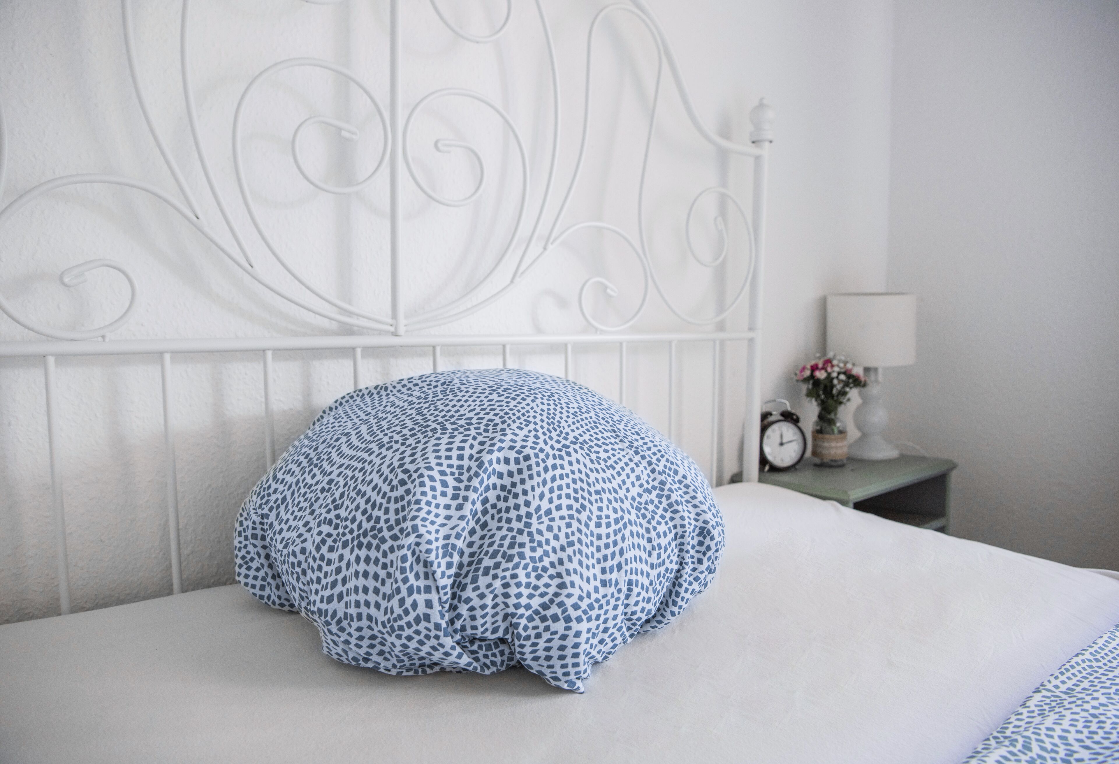 A neatly made bed with a patterned pillow and a white metal headboard.