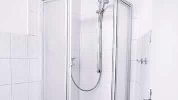 Box de chuveiro moderno com porta de vidro, chuveiro manual e um banquinho branco pequeno.