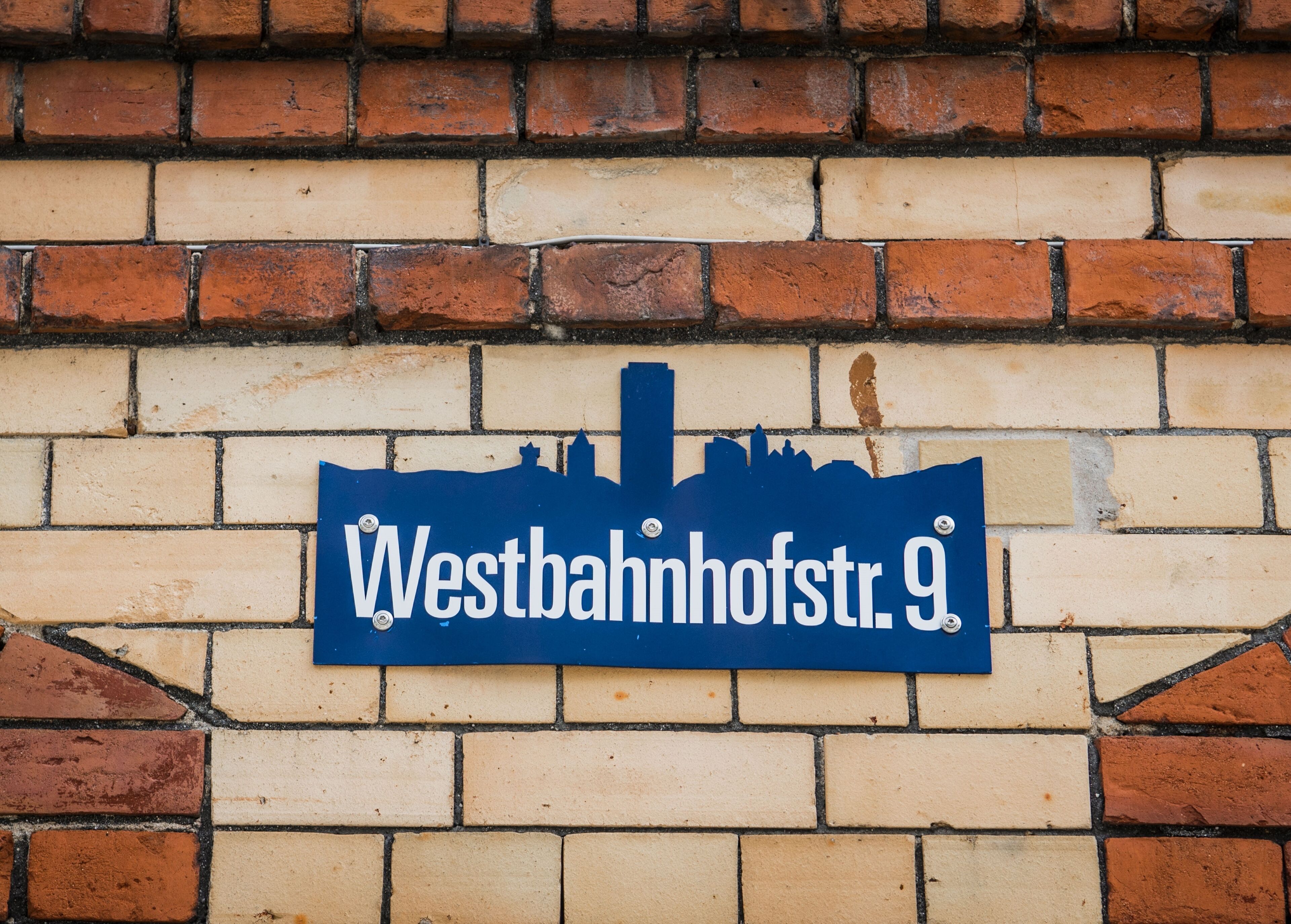 A street sign with the text "Westbahnhofstr. 9" mounted on a brick wall.