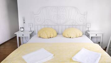 A neatly made bed with a yellow patterned bedspread, two pillows, and two folded white towels. There are two bedside tables with a small alarm clock and a lamp on each.