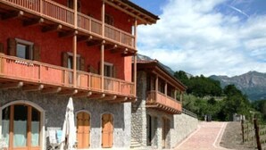 A multi-story building with balconies, stone walls, and a paved pathway leading to a mountainous landscape. - Maso Fiorini (Isera)