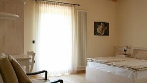 A bedroom with a wooden ceiling, a bed, a chair, a table, and a window with curtains. - Maso Fiorini (Isera)