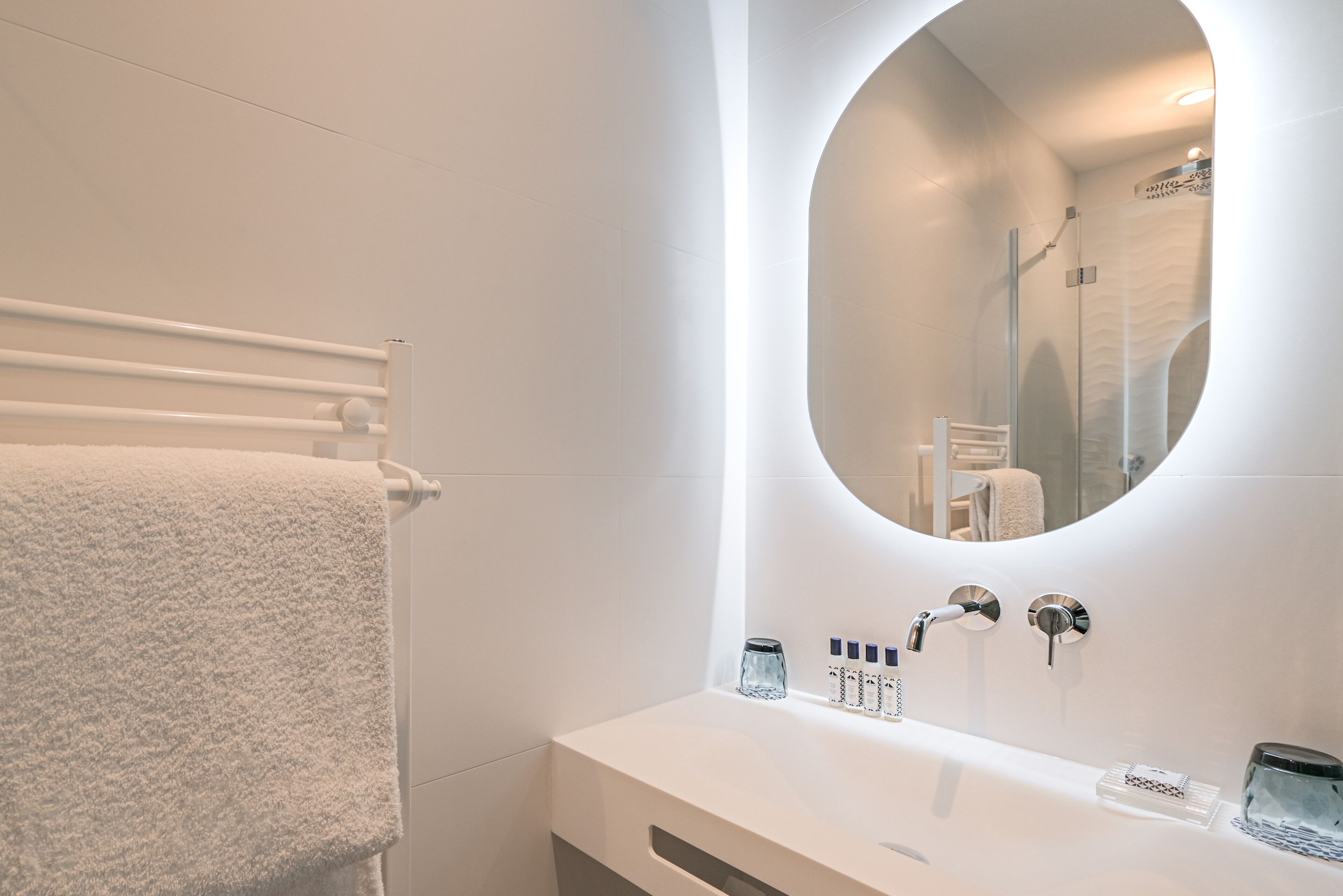 A modern bathroom with a white vanity, a large mirror, and a towel rack.