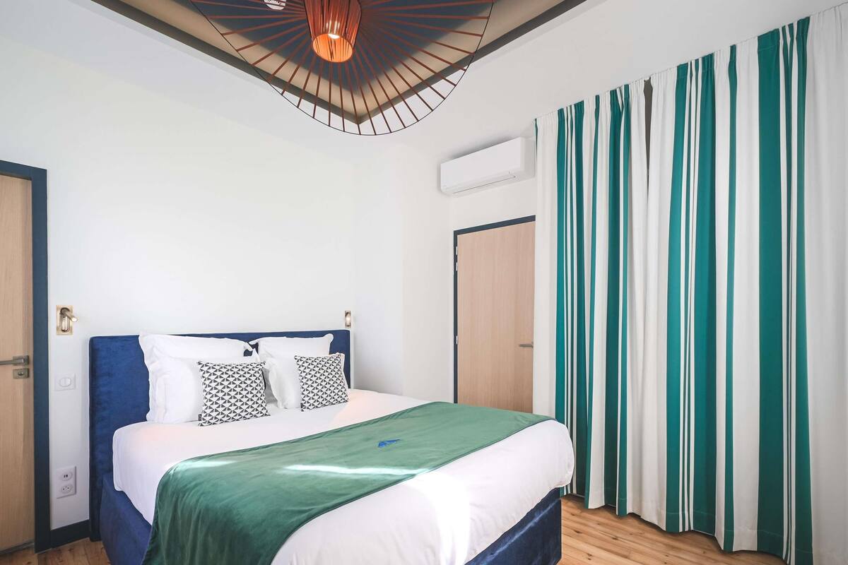A bedroom with a bed, a ceiling light fixture, an air conditioning unit, and a door.