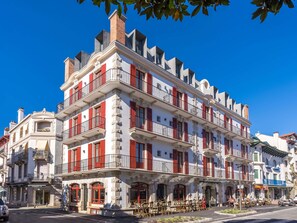 Ein mehrstöckiges Gebäude mit Balkonen, einem Café im Erdgeschoss und einer sichtbaren Schaufensterfront.