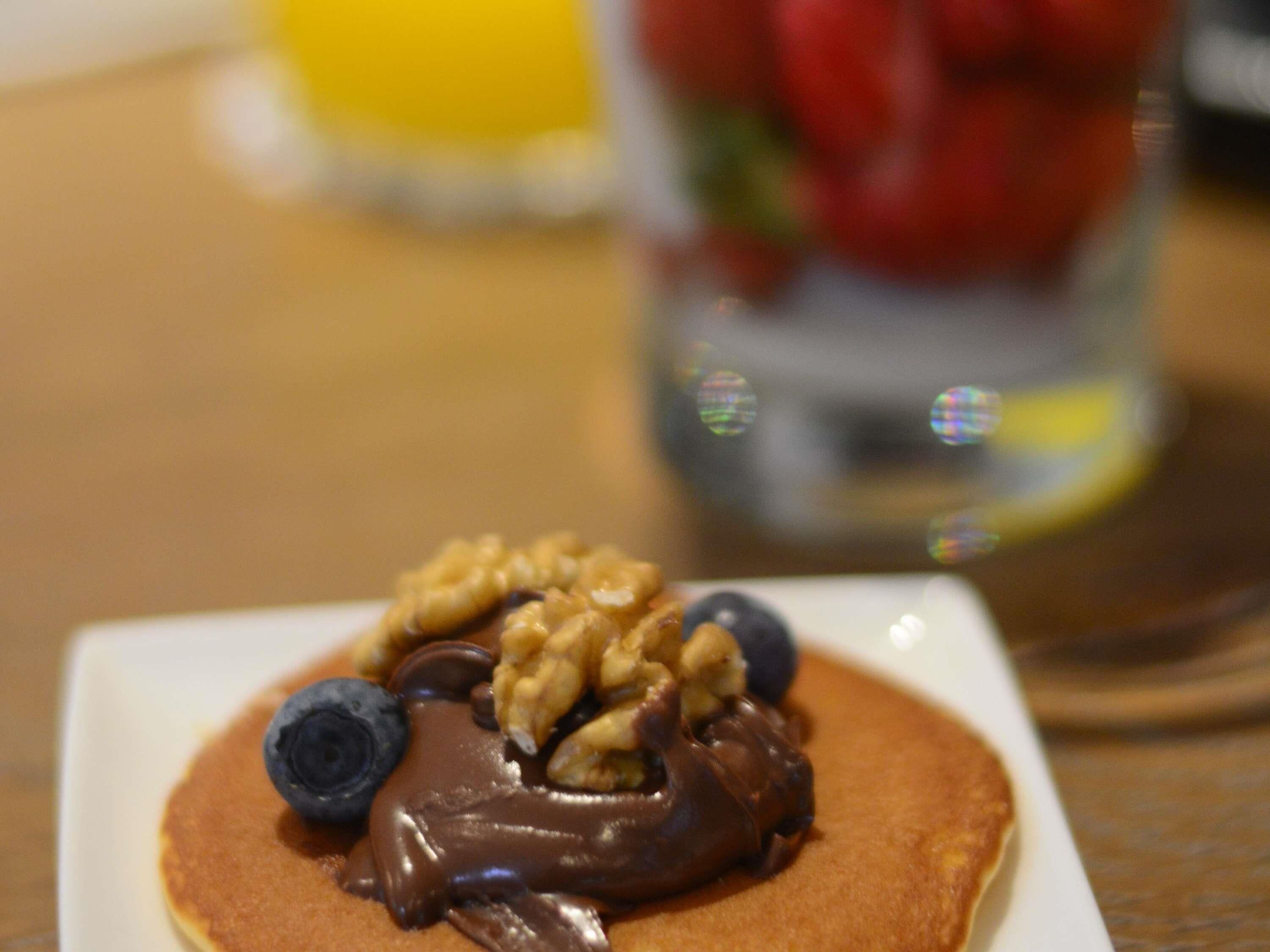 A plate with pancakes topped with chocolate sauce, walnuts, and blueberries.