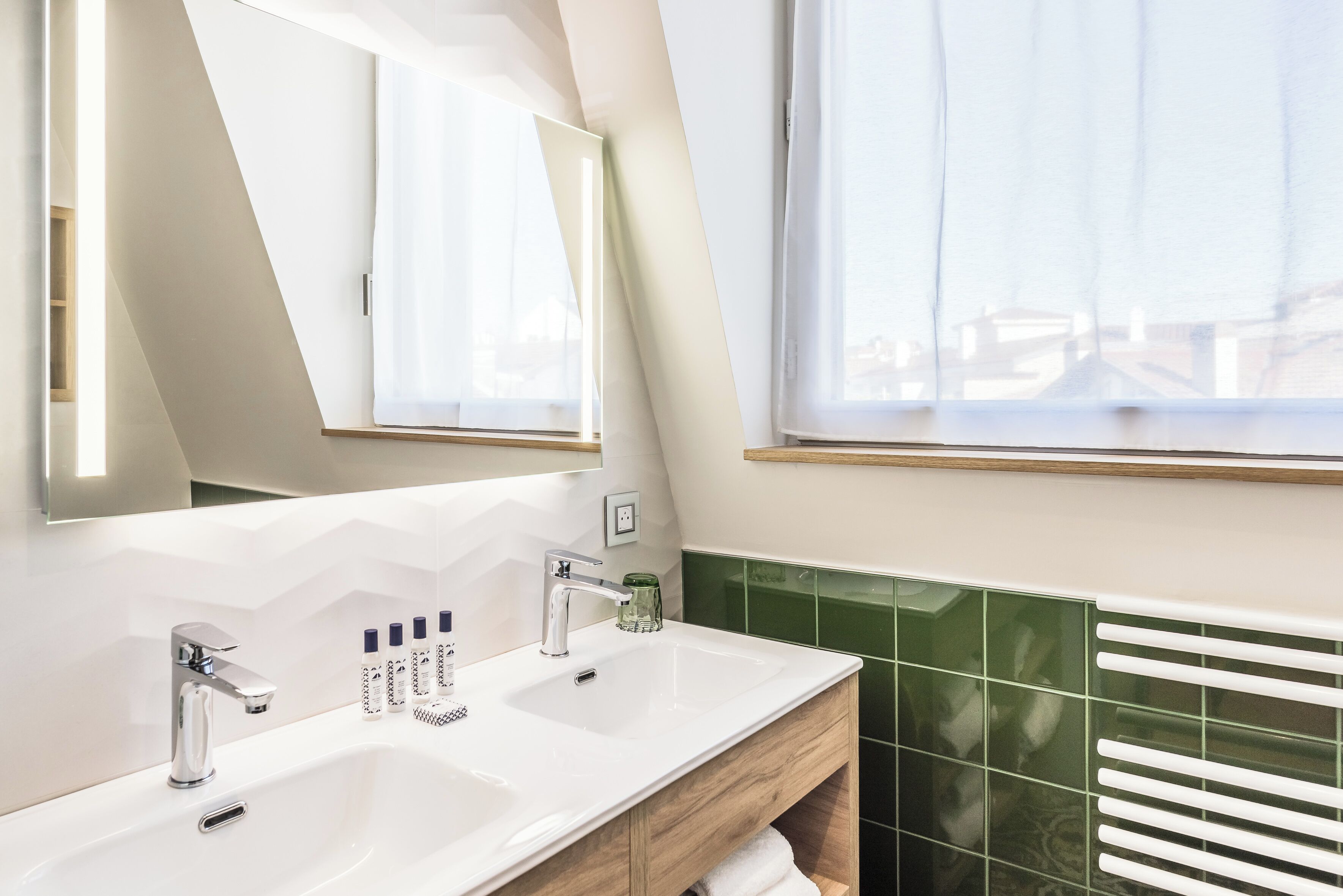 Un baño moderno con un espejo grande, dos lavamanos y una ventana con persianas.