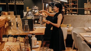A barista preparing drinks at a counter with a variety of coffee-making equipment and a patterned floor.