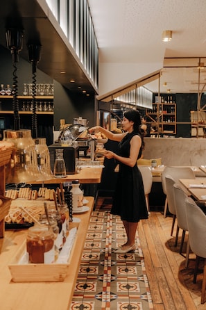 Un barista prépare des boissons derrière un comptoir équipé de divers appareils pour faire du café, et le sol est décoré de motifs.